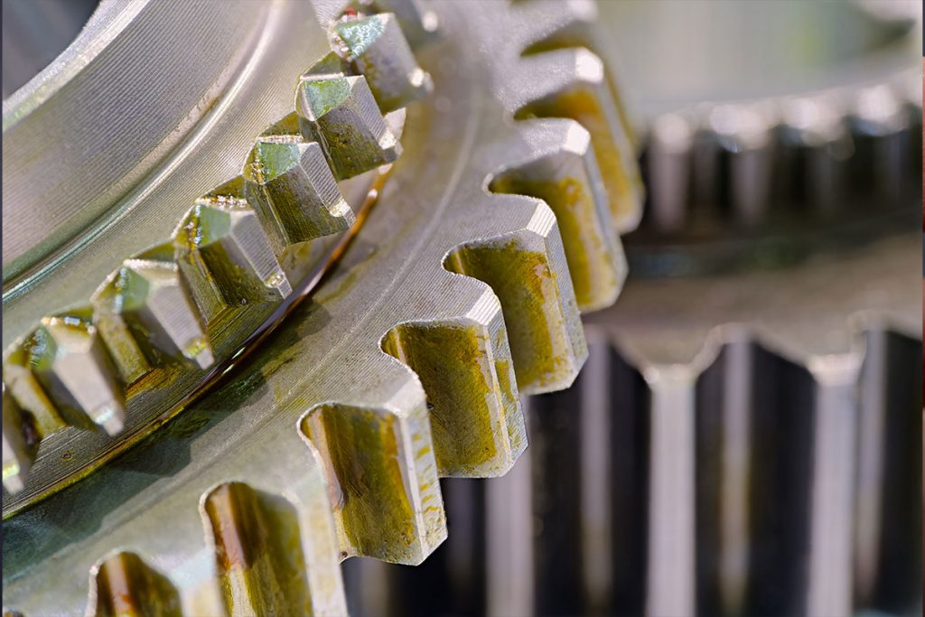 Nahaufnahme von zwei ineinander greifenden Metallzahnrädern mit sichtbaren Zähnen; die Zahnräder haben eine leicht abgenutzte und fettige Oberfläche, was auf eine in Betrieb befindliche Industriemaschine oder mechanische Ausrüstung schließen lässt.