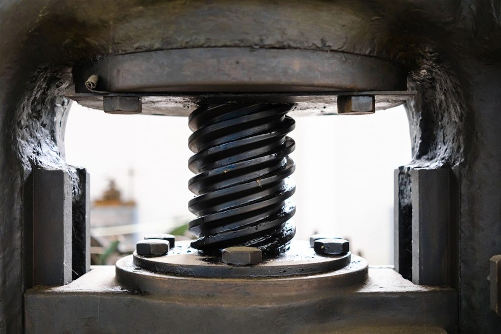 Nahaufnahme eines großen industriellen Gewindemechanismus aus Metall, wahrscheinlich Teil einer Hochleistungsmaschine oder -presse, mit im Vorder- und Hintergrund sichtbaren Bolzen und Metallflächen.